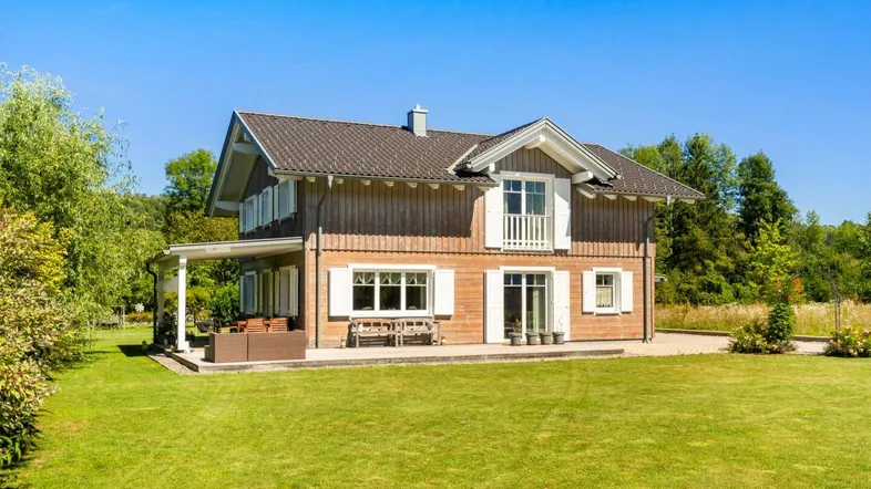 Charmantes Holzhaus mit großem Garten und überdachter Terrasse unter blauem Himmel.