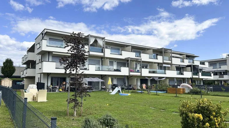Mehrfamilienhaus mit modernen Balkonen und gemeinschaftlicher Grünfläche mit Spielbereich.