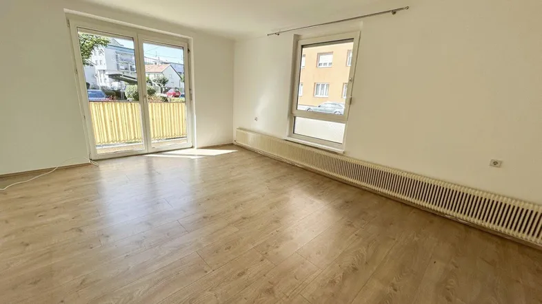 Helles Zimmer mit Laminatboden, weißen Wänden und Zugang zu einem kleinen Balkon.