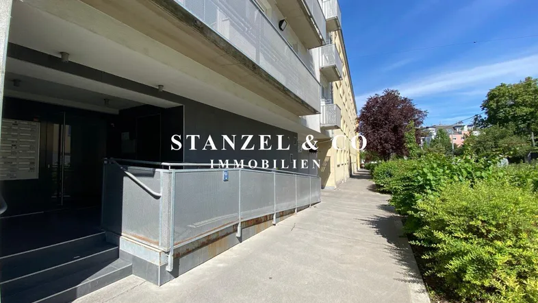 Eingangsbereich eines Mehrfamilienhauses mit Rampe und Treppe für barrierefreien Zugang.
