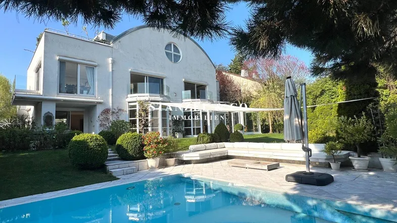 Elegante Hausfassade mit großem Garten, Pool und Terrasse, umgeben von üppigem Grün.
