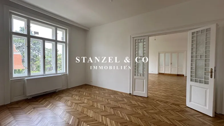 Helles Zimmer mit Fischgrätparkett, großem Fenster und Durchgang zu einem angrenzenden Raum.