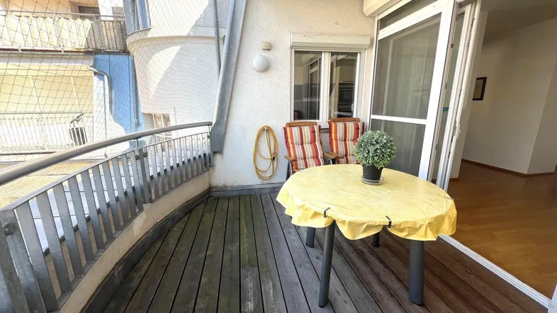 Möblierter Balkon mit Holzboden und Blick auf die umliegenden Gebäude.
