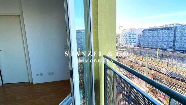 Blick vom Balkon auf die Stadt und Bahngleise, mit Zugang zu einem hellen Innenraum.