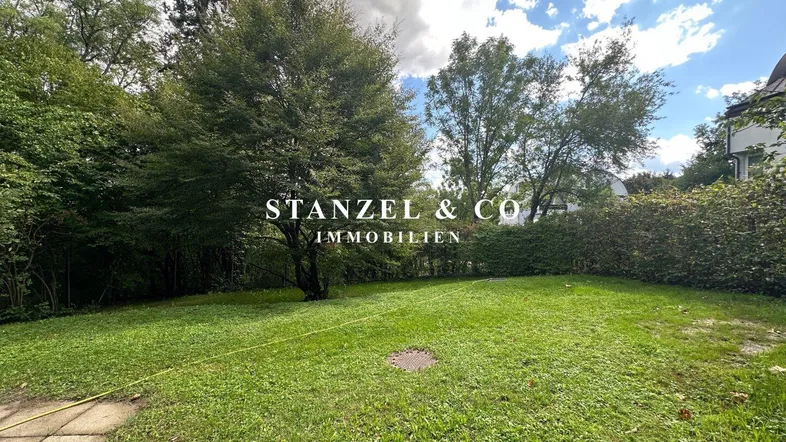 Weitläufiger, gepflegter Garten mit altem Baumbestand und viel Grünfläche unter blauem Himmel.