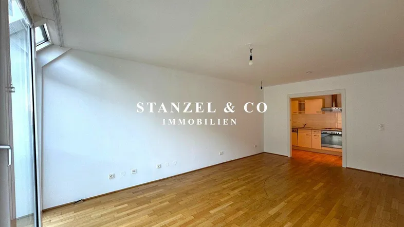 Geräumiges Wohnzimmer mit hellem Parkettboden und offenem Zugang zu einer separaten Küche.