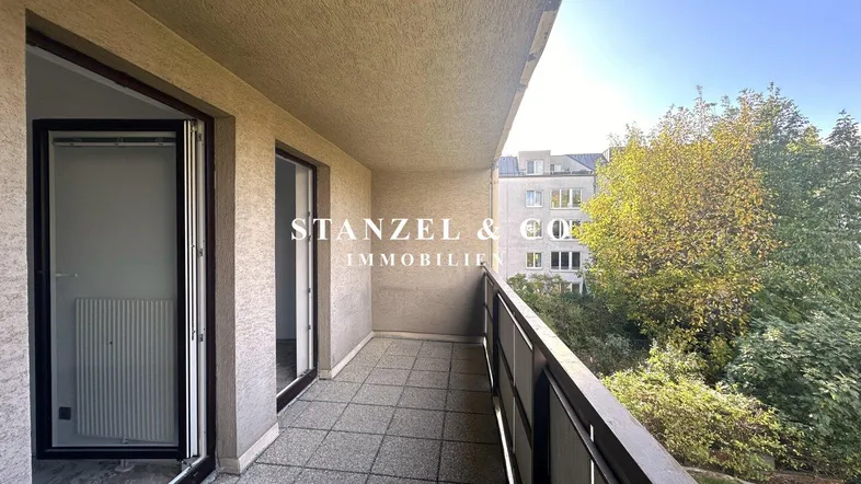 Geräumiger Balkon mit Fliesenboden und Blick auf die umliegende Bebauung und Bäume.