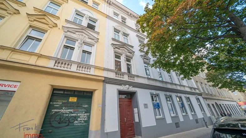 Historische Fassade eines Mehrfamilienhauses mit gelben und weißen Elementen an einer Stadtstraße.