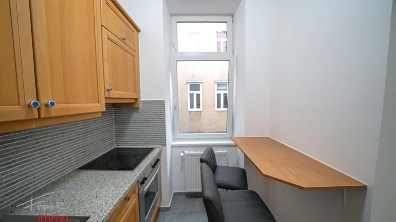 Funktionale Küche mit hellen Holzschränken, Granitarbeitsplatte und einem kleinen Esstresen am Fenster.