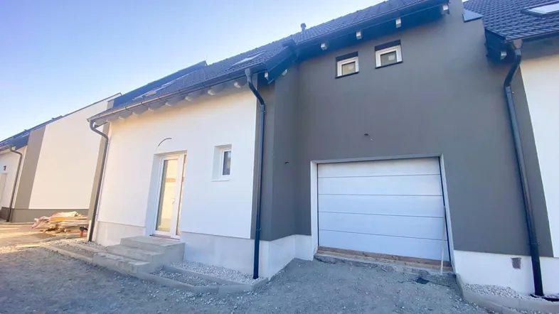 Neubau-Reihenhaus mit moderner Fassade und integrierter Garage unter blauem Himmel.