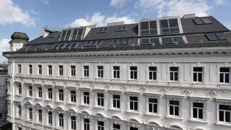 Obere Etagen eines eleganten Gebäudes mit vielen Dachfenstern und klassischer Fassade.