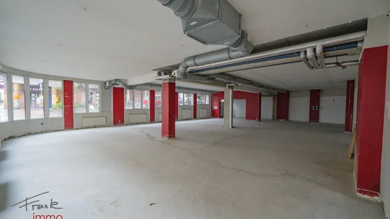 Großer, offener Gewerberaum mit roten Säulen, sichtbaren Lüftungsrohren und vielen Fenstern zur Straße.