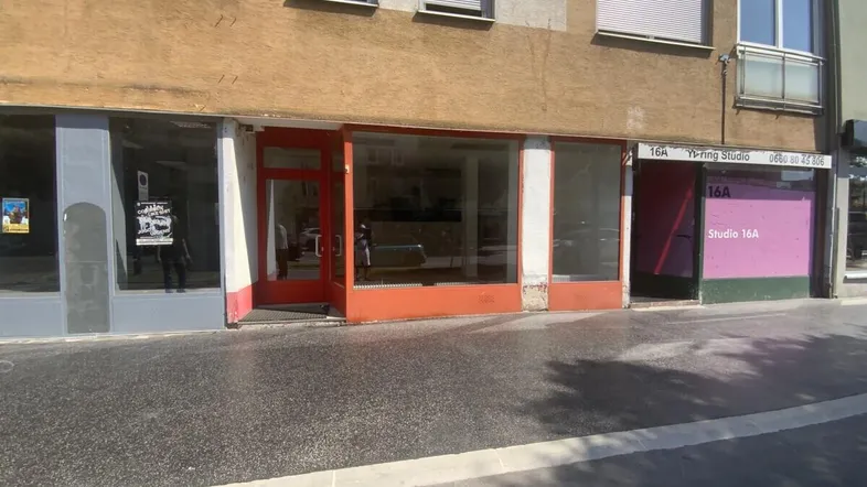 Außenansicht eines Gebäudes mit mehreren Ladenfronten, darunter ein offener Eingang und eine verkleidete Fläche.