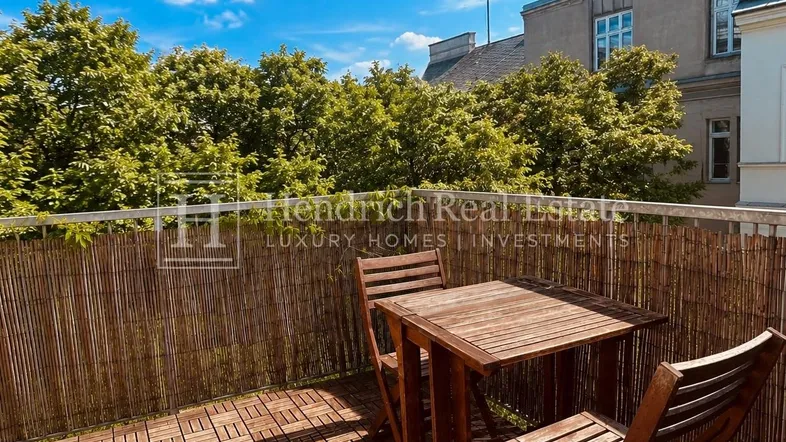 Gemütlicher Balkon mit Holzbodenfliesen, Sitzgelegenheiten und Blick auf grüne Bäume.