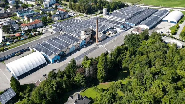 Weitläufige Luftaufnahme eines Industrieparks mit zahlreichen Gebäuden, Solaranlagen und umgebenden Grünflächen.