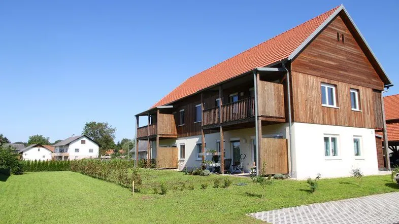 Modernes Mehrfamilienhaus mit Holzfassade, Balkonen und grüner Umgebung.