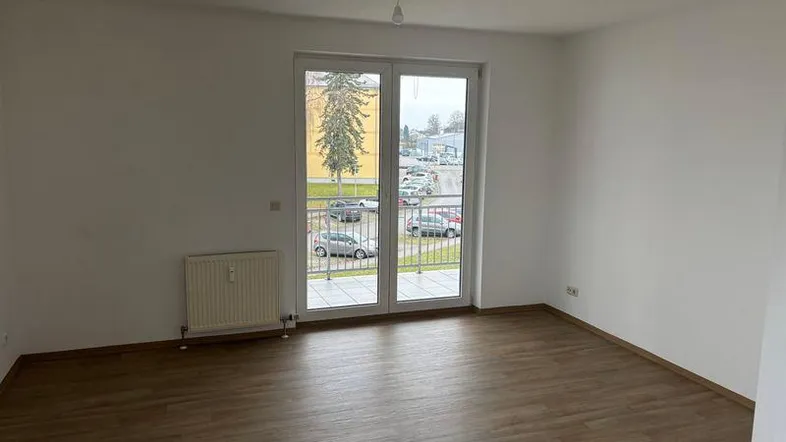 Helles Zimmer mit Laminatboden und Zugang zu einem Balkon, ideal als Wohn- oder Schlafzimmer.