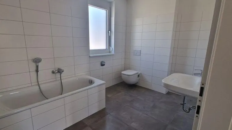 Helles Badezimmer mit Badewanne, WC, Waschbecken und Fenster für Tageslicht.