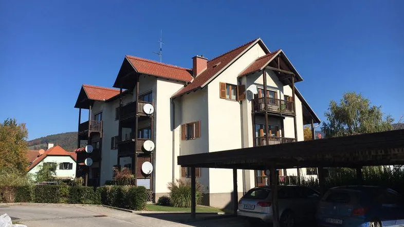 Mehrfamilienhaus mit Satteldach, Balkonen und überdachten Stellplätzen im Freien.