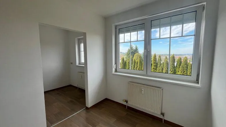 Helles Zimmer mit Holzboden und weitem Blick ins Grüne, verbunden mit einem weiteren Raum.