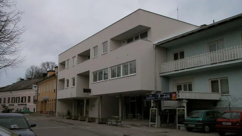 Modernes Gebäude mit Flachdach und großen Fenstern an einer Straße mit weiteren Häusern.