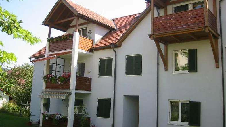 Charmantes Mehrfamilienhaus mit weißer Fassade, Holzverkleidungen und mehreren Balkonen im Grünen.