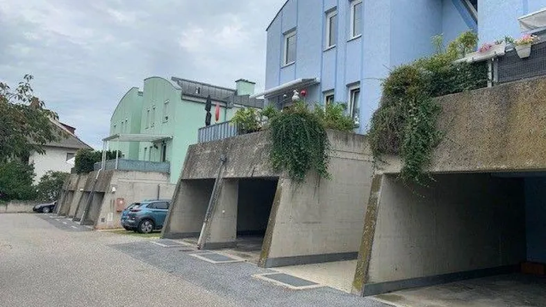 Mehrere Gebäude mit blauer und grüner Fassade sowie integrierten Garagenstellplätzen und begrünten Balkonen.
