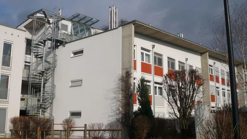 Modernes Mehrfamilienhaus mit weißer Fassade, roten Akzenten und einer auffälligen Außentreppe.