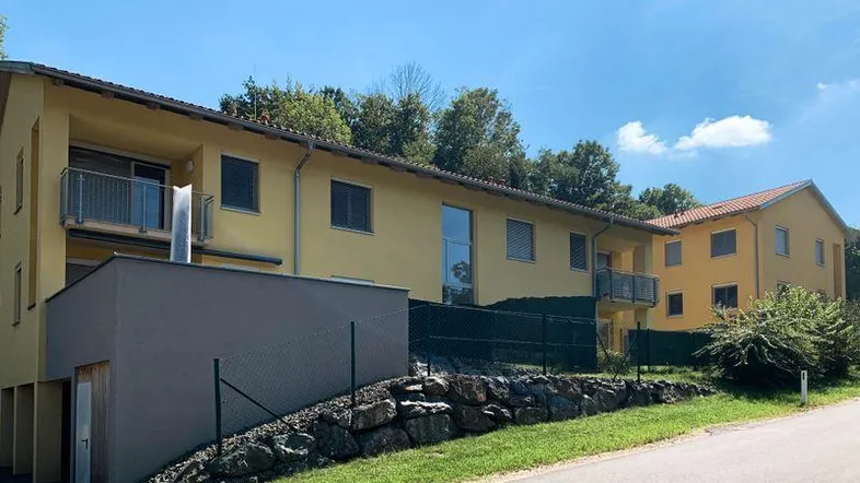 Mehrere moderne Gebäude mit gelber Fassade und Balkonen in ländlicher Umgebung mit viel Grün.