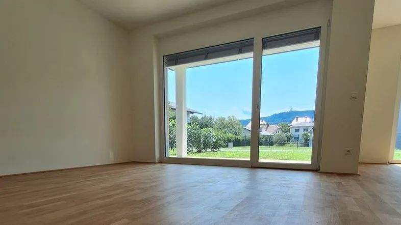 Heller Wohnraum mit großen Fenstern, Holzboden und Blick ins Grüne sowie auf die umliegende Landschaft.