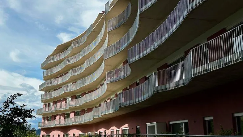 Moderne Wohnanlage mit geschwungenen Balkonen und einer markanten rosa Fassade unter bewölktem Himmel.