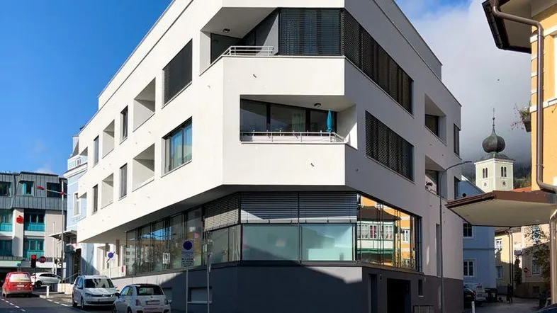 Modernes Mehrfamilienhaus mit weißer Fassade, großen Fenstern und Balkonen in städtischer Umgebung.