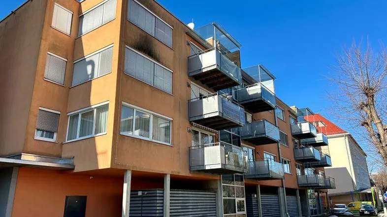 Mehrfamilienhaus mit orangefarbener Fassade, modernen Balkonen und Außenjalousien unter blauem Himmel.