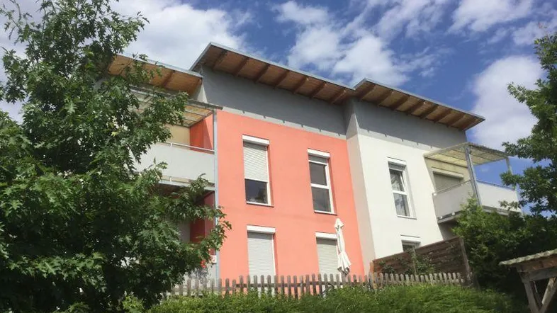 Modernes Wohngebäude mit orangefarbener und grauer Fassade, Balkonen mit Pergolen und Rollläden.