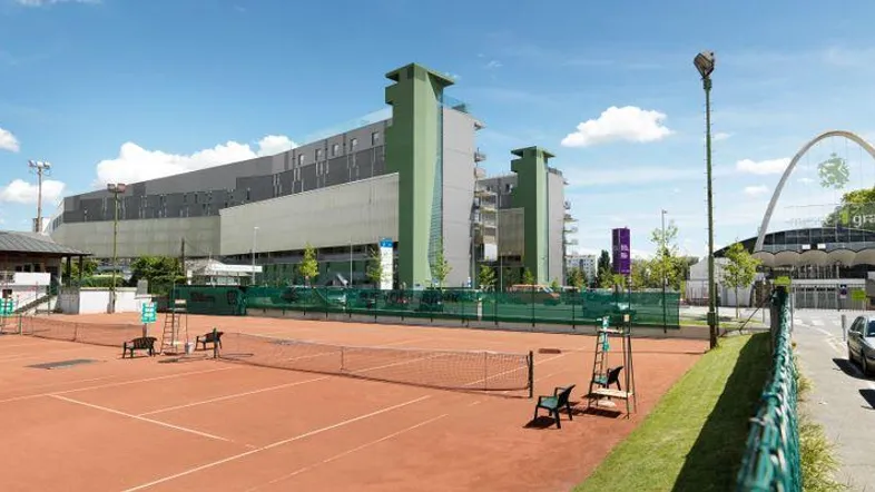 Außenansicht eines modernen Gebäudes mit angrenzenden Tennisplätzen unter blauem Himmel.