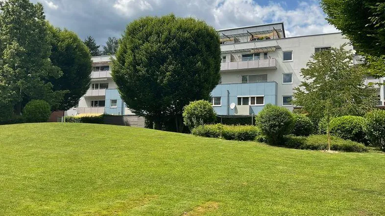 Mehrfamilienhaus mit gepflegter Grünfläche und Balkonen unter bewölktem Himmel.
