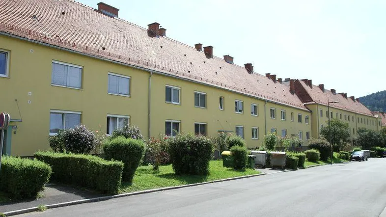 Eine Reihe von Wohngebäuden mit gelber Fassade und roten Ziegeldächern entlang einer ruhigen Straße.