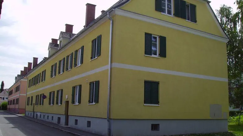 Gelbes Mehrfamilienhaus mit Mansarddach und grünen Fensterläden in gepflegtem Zustand.