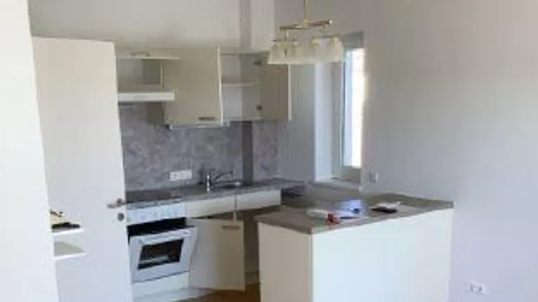 Helle Küche mit weißen Schränken, integriertem Backofen und Holzboden, ideal für den täglichen Gebrauch.