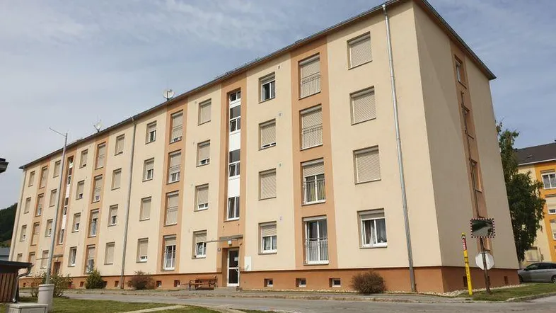 Gepflegtes Mehrfamilienhaus mit beiger Fassade und Rollläden an den Fenstern unter bewölktem Himmel.