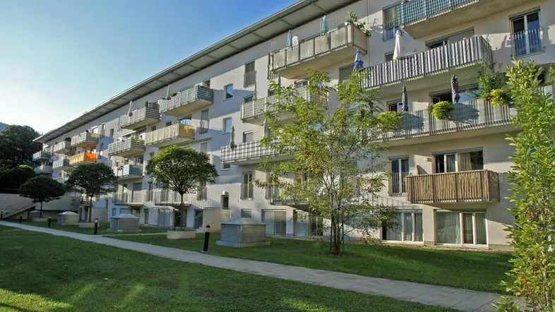 Mehrfamilienhaus mit zahlreichen Balkonen und gepflegter Grünfläche im Außenbereich unter blauem Himmel.