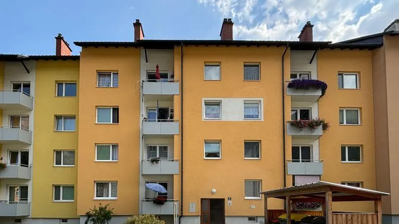 Mehrfamilienhaus mit gelber Fassade, mehreren Balkonen und einem kleinen Vorgartenbereich.