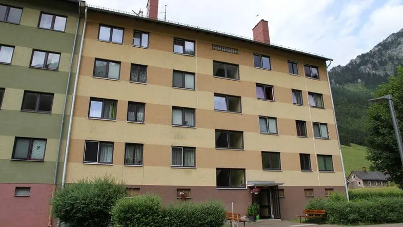 Mehrfamilienhaus mit gestreifter Fassade und grüner Umgebung vor einer beeindruckenden Bergkulisse.