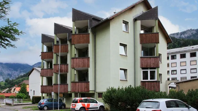 Mehrstöckiges Apartmentgebäude mit Balkonen und Blick auf die umliegende Berglandschaft.