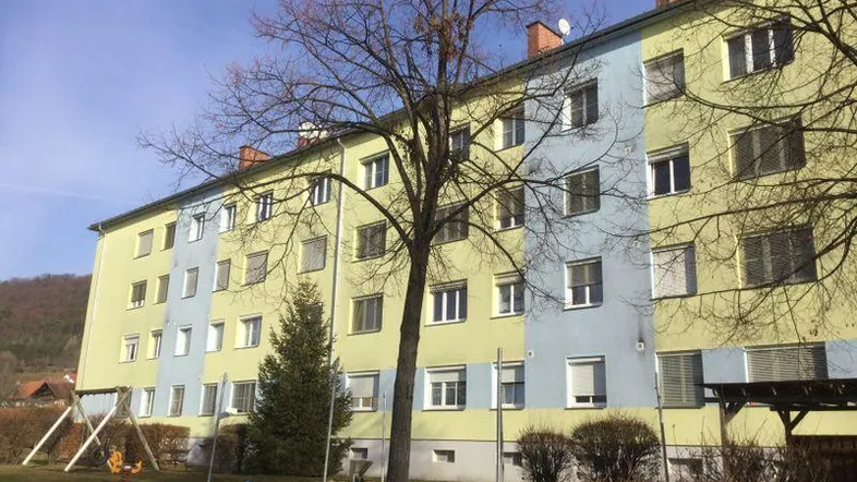 Mehrfamilienhaus mit farbiger Fassade, Spielplatz und Blick auf die grüne Umgebung.