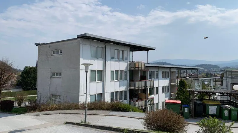 Mehrfamilienhaus mit mehreren Balkonen und Blick auf die umliegende Landschaft und Berge.