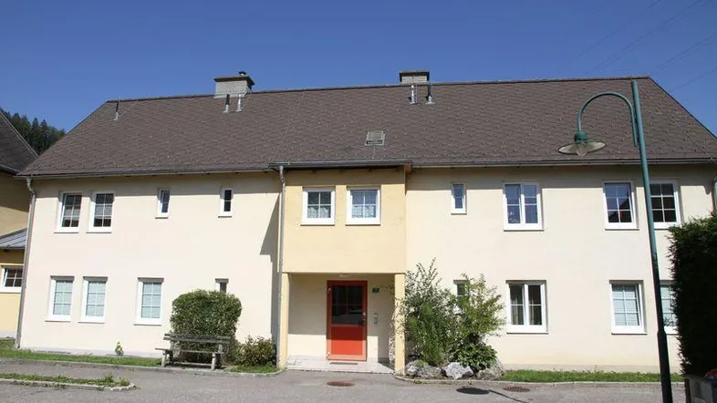 Gepflegtes Mehrfamilienhaus mit heller Fassade, Satteldach und Parkplätzen im Freien an einem sonnigen Tag.