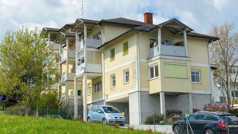 Mehrfamilienhaus mit mehreren Balkonen, Carport-Stellplätzen und gepflegter Fassade in grüner Umgebung.