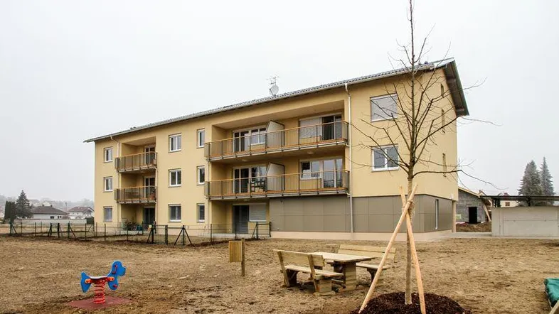 Neues Mehrfamilienhaus mit Balkonen, umgeben von einer Grünfläche mit Spielgeräten und Sitzgelegenheiten.
