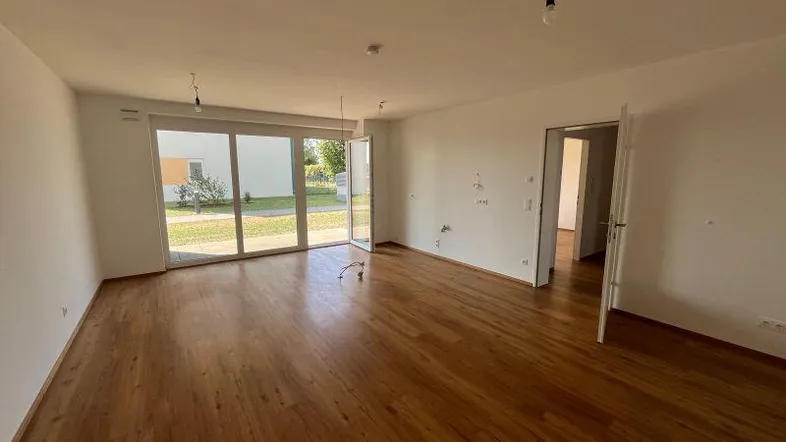 Heller Raum mit Holzboden und großen Glasschiebetüren, die Zugang zum Gartenbereich bieten.